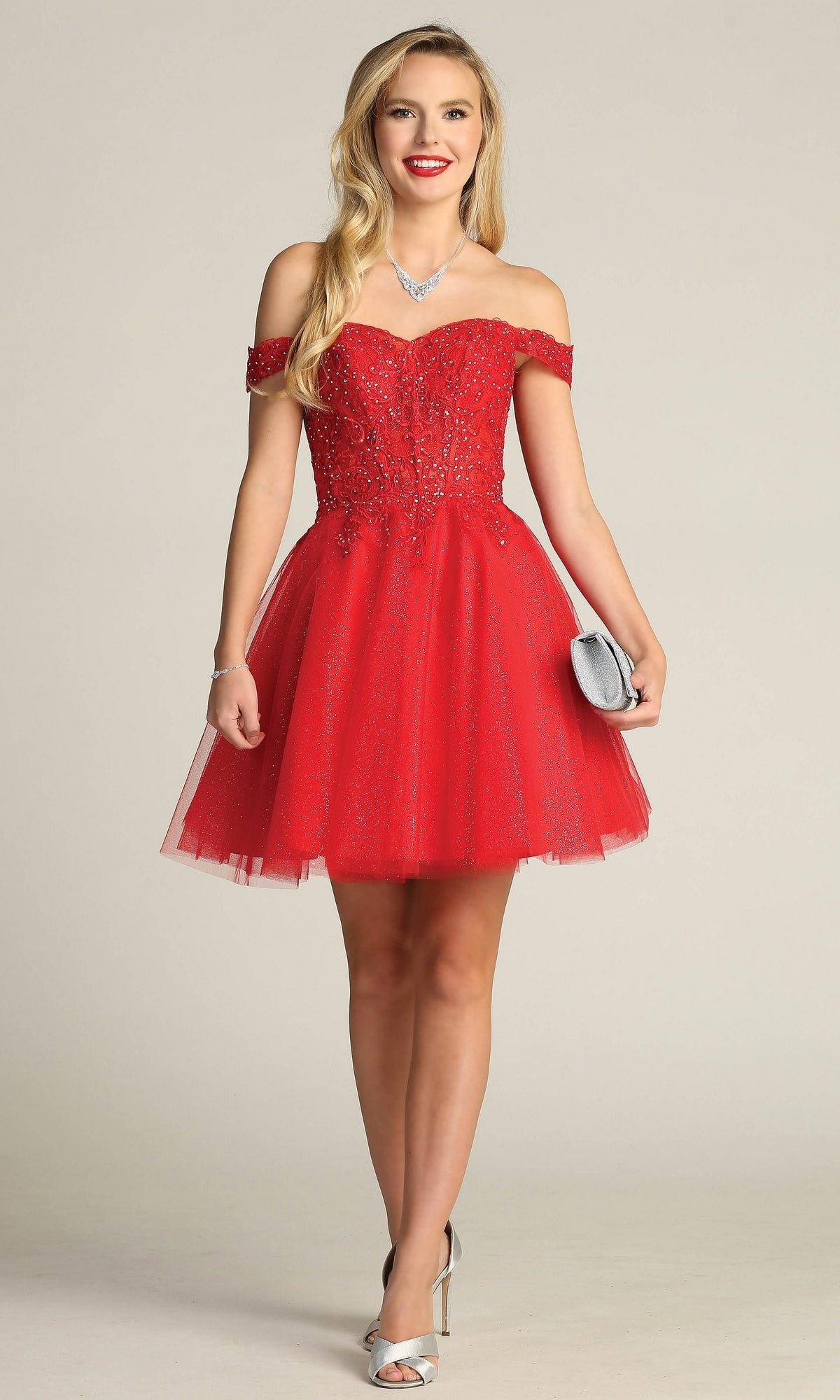A woman wearing the Off-Shoulder Short Glitter Homecoming Dress C318 with bead embellishments, silver high heels, a necklace, and holding a silver clutch stands against a plain background.